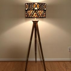 a lamp that is sitting on top of a wooden tripod in front of a wall