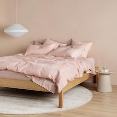 a bed sitting on top of a wooden floor next to a white rug and light pink walls