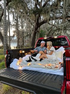 a man and woman sitting in the back of a truck with lights on it's bed