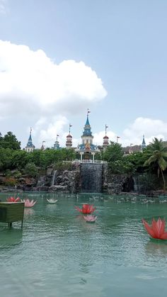 there are many red flowers floating in the water near a waterfall and some blue buildings