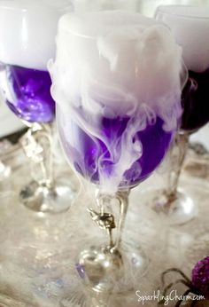 three wine glasses with liquid in them sitting on a silver tray next to purple and white decorations