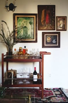 a table with wine glasses and bottles on it in front of pictures hanging on the wall