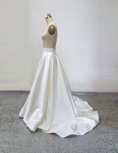 a white wedding dress on display in front of a white wall and grey flooring