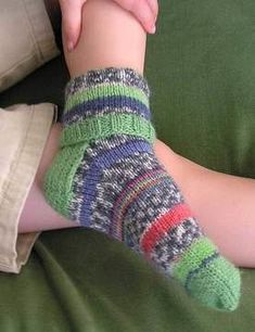 a child's legs with socks on sitting on top of a green couch next to pillows