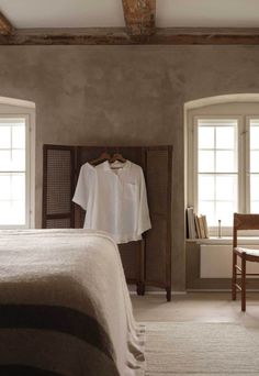 a bedroom with a white shirt hanging on a clothes rack next to a bed and two windows