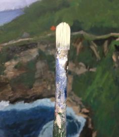 the paintbrush has been painted with watercolors on it and is next to an ocean