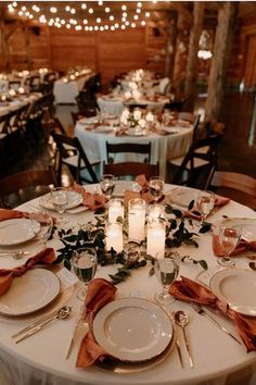 the table is set with white plates and silverware, candles, and greenery