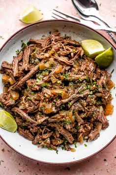 a white bowl filled with shredded beef and garnished with cilantro, lime wedges