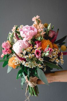 a bouquet of flowers is being held by someone's hand in front of a gray wall