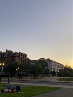 two people laying on the grass in front of an old building at sunset or dawn