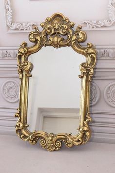 an ornate gold framed mirror in front of a white painted wall with decorative moldings