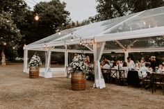 a group of people sitting at tables under a tent with white drapes and lights