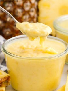 a spoon full of pineapple pudding on top of a plate with sliced pineapples