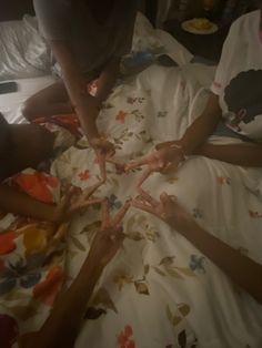 four people sitting in a circle on top of a bed with white sheets and flowers