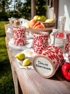 red and white cups sitting on top of a wooden table next to apples, lemons and an apple cider