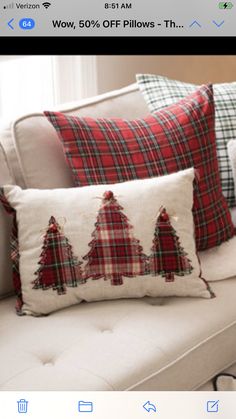 two christmas pillows on a couch with plaid and red trees embroidered on them, one in the shape of an xmas tree