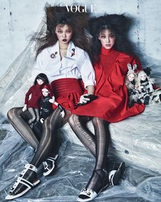 two young women sitting on top of each other in front of a white wall with black and red accessories