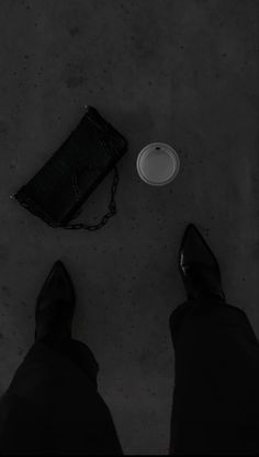 a person standing next to a black purse and a white plate on the ground with their feet up