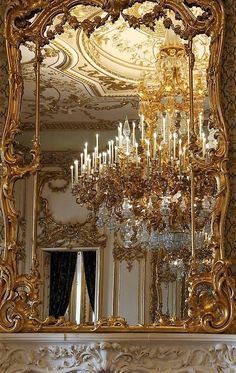 an ornate gold mirror with chandelier hanging from it's sides in front of a fireplace