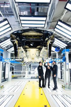 two men standing in front of an assembly line looking at something on the floor that is being worked on