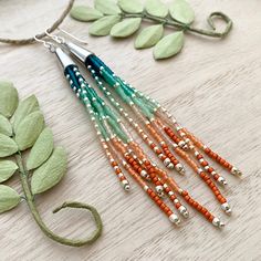 an assortment of different colored beads hanging from a string on a wooden table next to leaves