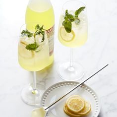 two glasses filled with lemonade and mint on top of a white plate next to a bottle