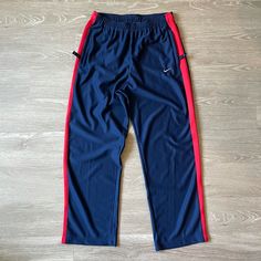 This Fresh Pair Of Nike Solid Swoosh Stripe Pant Is Made From A Lightweight Cozy Knit Satin Jersey Fabric, Keeping You Warm While Looking Dope At All Times. The Midnight Navy Blue Pant Features A Contrasting Red Stripe On The Side, With Minor Usa Flag Above The Back Pocket (Which Is Closable With A Zipper). The Nike Solid Swoosh Stripe Pant Has Two Side Pockets To Store All You Smaller Belongings Like Phone Or Wallet. - Elastic Waistband With Drawcord - Zippered Front Pockets - 100% Polyester Blue Wide Leg Sportswear Pants, Sporty Blue Pants With Straight Hem, Nike Sporty Navy Pants, Sportswear Wide Leg Blue Bottoms, Blue Wide Leg Sportswear Bottoms, Red Nike Cotton Sweatpants, Red Cotton Nike Sweatpants, Nike Red Athleisure Pants, Sporty Red Straight Leg Bottoms