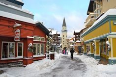 people are walking down a snowy street lined with buildings