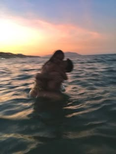 two people are hugging in the water at sunset or dawn, while one person is on his back