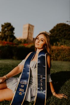 a woman sitting in the grass wearing a blue and gold sash with her name on it