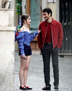 a man standing next to a woman on a street talking to each other and smiling