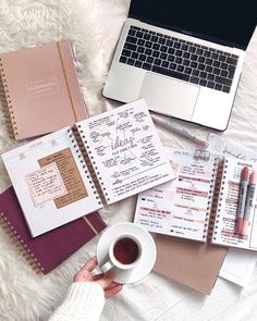 a person holding a cup of coffee next to notebooks and a laptop