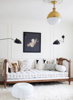 a white day bed with pillows on it in front of a wall and a painting