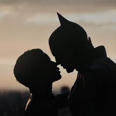 the silhouette of two people kissing each other in front of a cityscape at sunset