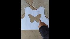 someone cutting out a paper butterfly on top of a white tank top with scissors next to it