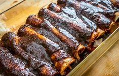 barbecue ribs covered in bbq sauce sit in a baking pan on a wooden table