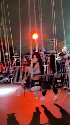 two women sitting on swings at night with people standing around and watching from behind them