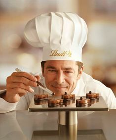 a man in a chef's hat is holding a spoon and looking at small chocolates on a plate