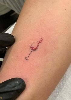 a woman's arm with a small tattoo of a wine glass and a corkscrew