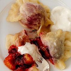 a white plate topped with dumplings covered in sauce and fruit next to a fork