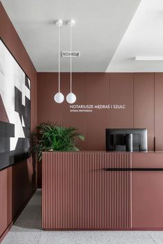 the front desk of an office with pink walls and black counter tops, along with two hanging lights