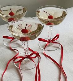 three martini glasses with cherries in them on a white tablecloth and red ribbon