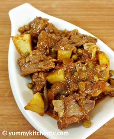 a white plate topped with meat and potatoes on top of a wooden table next to a fork