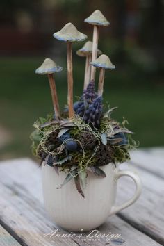 a white cup filled with plants and mushrooms on top of a wooden table