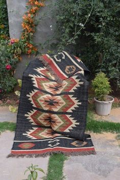 an old rug is laying on the ground in front of some plants and flowers,