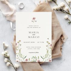 a wedding card with flowers on it sitting next to some napkins and white flowers