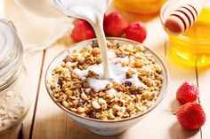 a bowl filled with granola and yogurt being poured into it next to strawberries