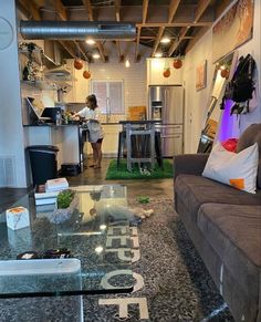 a woman standing in a kitchen next to a living room with a couch and coffee table