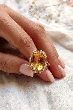 "A truly majestic engagement ring, with a beautiful round cut citrine and 14k gold. The center stone is surrounded by halo diamonds, featuring a smooth band, clean and gold. An imaginative look you'll adore, this ring is unsurpassed with magnificence and sparkle. ✦ Please send us your size (3-13 US). ✦ Details - Pendant Measurements: Height: 0.79 Inc'' / 20 mm Width: 0.63 Inc\" / 16 mm -Diamond weight: 0.30 carat -Diamond color: G-H -Diamond Clarity: VS1 -Receive diamond certification with your Yellow Oval Topaz Ring In 14k Gold, Elegant Citrine Diamond Ring With Halo Setting, Elegant Yellow Halo Ring With Center Stone, Oval Yellow Diamond Promise Ring, Oval Yellow Gold Diamond Halo Ring, Yellow Topaz Ring With Halo Setting For Wedding, Yellow Halo Rings Fine Jewelry, Yellow Rings With Halo Design As Gift, Yellow Rings With Halo Design For Gifts