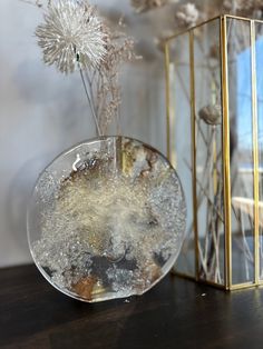 a glass vase filled with water next to a golden box and dried flowers on a table